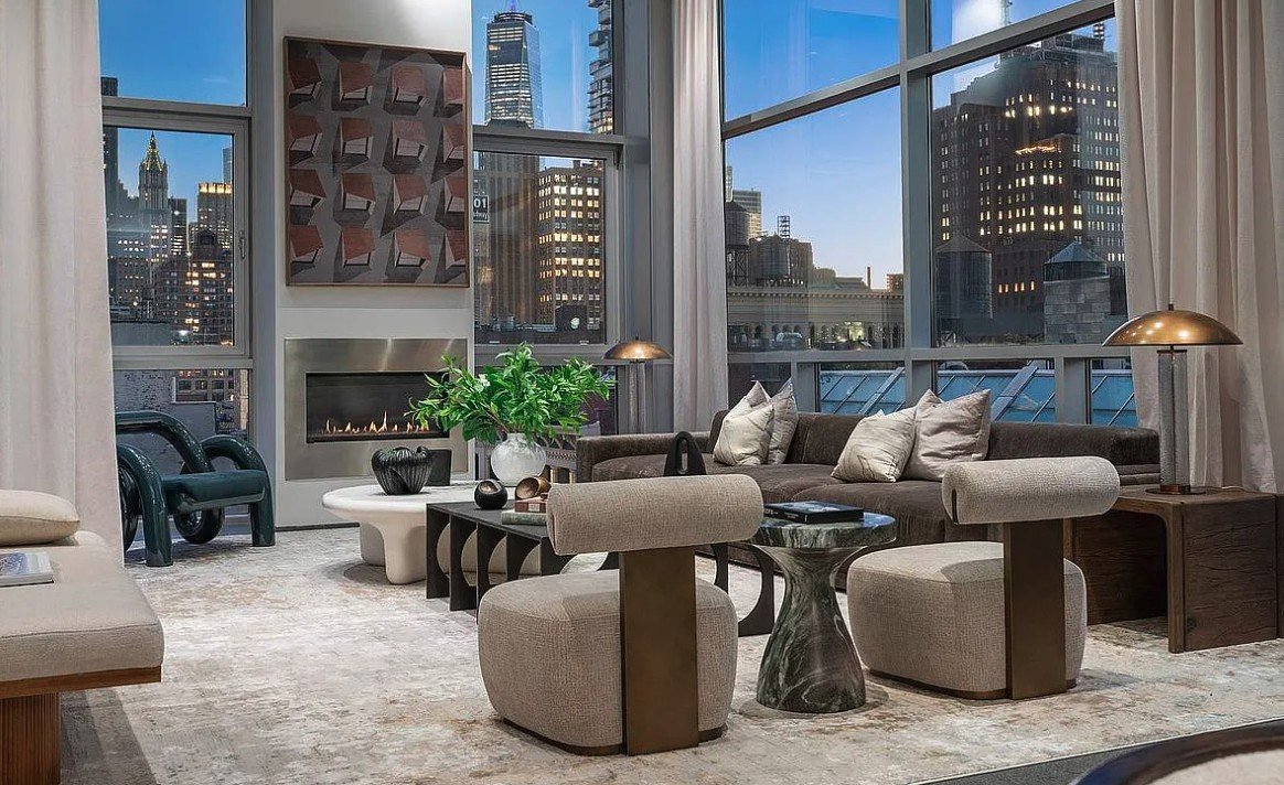 Living room at dusk with a gas fireplace, floor-to-ceiling windows and lit skyline views